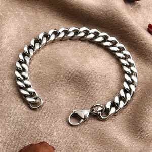 Detail shot of a silver Cuban link bracelet with a lobster clasp on silk fabric