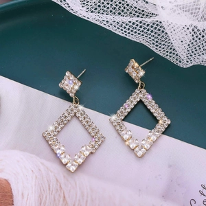 Elegant geometric rhombus gold earrings with sparkling crystals on green tray background