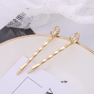 Macro view of gold wave hair clips with rectangular zircon stones on a ceramic plate