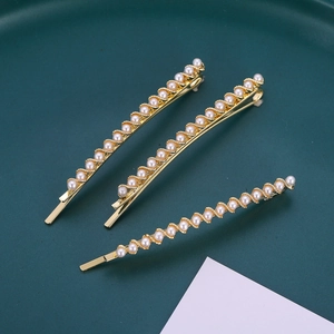 Set di tre eleganti fermagli per capelli dorati con perle bianche su un vassoio verde