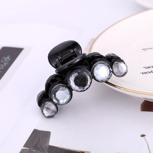 Detail of a black hair claw clip featuring sparkling crystals on a ceramic dish background