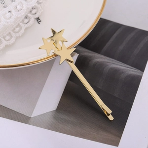 Fermaglio per capelli minimalista in metallo dorato con tre stelle su un piatto bianco
