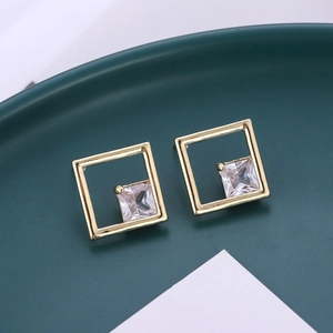 Macro shot of gold geometric square stud earrings with clear zircon on ceramic tray