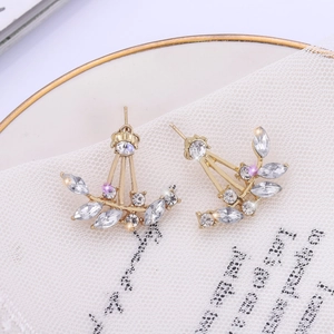 Detailed close-up of golden leaf-shaped earrings with sparkling zircon crystals on white lace