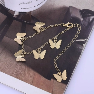 Elegant gold metal butterfly anklet with five textured charms on a stylish magazine backdrop