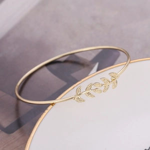 Elegant gold leaf open bangle bracelet with detailed leaf texture on white jewelry plate
