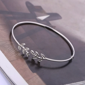 Elegant silver open bangle featuring leaf design on a stylish magazine backdrop