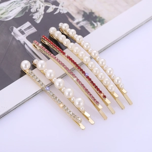 Five-piece set of gold hair pins with white pearls and colorful rhinestones on a magazine