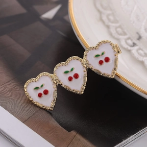 Barrette dorée élégante avec cœurs en émail blanc et motifs cerises sur un magazine