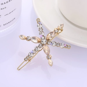 Elegant gold metal snowflake hair clip with champagne crystals on a white ceramic tray