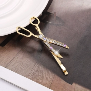 Pince à cheveux créative en forme de ciseaux dorés avec strass blancs et mauves sur plat