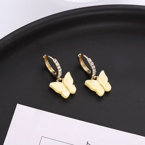 Vue macro de boucles d'oreilles dorées avec strass brillants et pendentif papillon crème