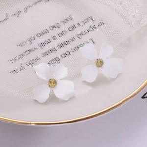 Macro detail of white four-petal flower earrings with golden core on lace cloth