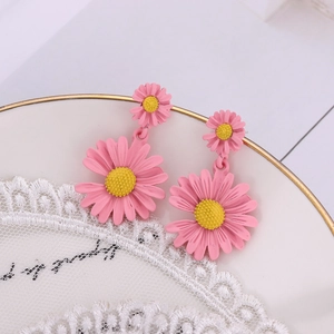 Détail de boucles d'oreilles marguerites roses et jaunes sur dentelle et céramique