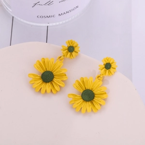 Détail de boucles d'oreilles marguerites jaunes à double fleur sur un support blanc