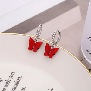 Close-up of red butterfly pendant earrings with sparkling diamonds on a white tray