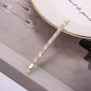 Elegante pasador de pelo dorado con circonitas rectangulares brillantes sobre fondo mármol