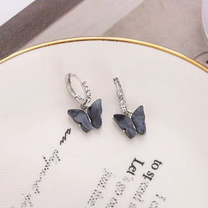Macro view of butterfly pendant earrings with crystal-inlaid hoops on white display tray