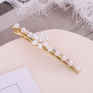 Détail d'une barrette dorée ornée de perles blanches et de motifs floraux en strass brillants