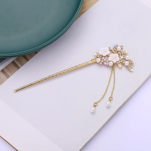 Elegant gold hair pin with white flowers, pearls, and tassels in a minimalist setting