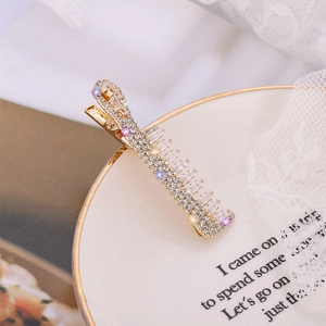 Barrette dorée élégante ornée de cristaux blancs et violets sur un plat en céramique