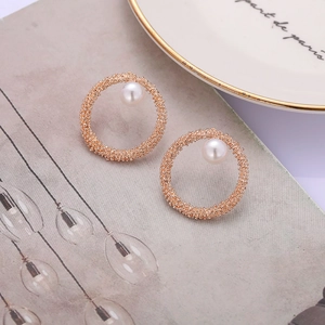 Close-up of C-shaped rose gold pearl earrings with textured finish on magazine background