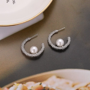 Detail of silver C-shape earrings with textured frosted finish and white pearls
