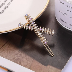 Modieuze gouden K-letter haarclip met paarse en witte strasstenen op een magazine