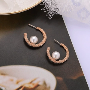 Close-up of rose gold C-shaped pearl earrings with granular texture on vintage book background