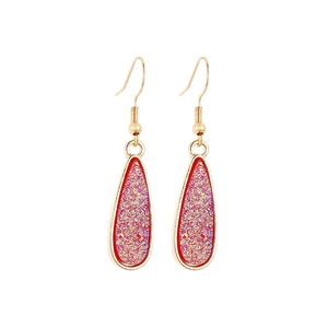 Detailed close-up of golden teardrop earrings with sparkling pink crystal inlay and red trim