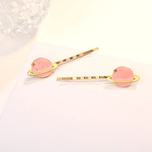 Barrettes à cheveux planète dorées avec émail rose et anneaux sur un socle blanc