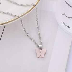 Détail du collier chaîne torsadée argentée avec pendentif papillon rose sur plateau blanc