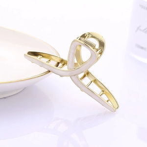 Detail of a large gold alloy hair claw clip with white enamel finish on a porcelain plate