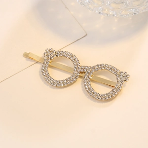 Pince à cheveux lunettes dorées ornée de strass brillants sur un fond beige élégant