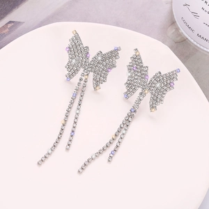 Détail de boucles d'oreilles papillon à pompons avec strass blancs et violets brillants
