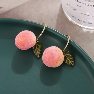 Pink velvet peach earrings with gold hoop and green leaf on elegant dark green plate