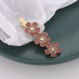 Detail einer Haarspange mit rosa Kristallblumen und goldener Basis auf grünem Tablett
