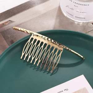 Elegant gold metal hair comb with wavy texture placed on a green ceramic dish