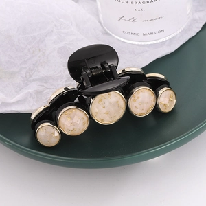 Elegant black hair claw clip with gold foil marble button accents on dark green tray