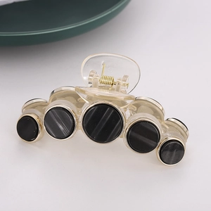 Retro clear acrylic hair claw with five gold-rimmed black circular accents on grey background
