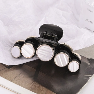Detail of black hair claw clip featuring five pearl-like shell accents and gold metal trim