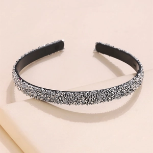 Detail view of a slim crystal headband with sparkling silver rhinestones on a beige background