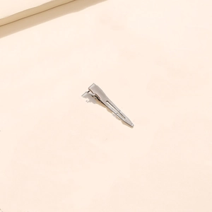 Close-up of minimalist silver metal duckbill hair clip on a beige neutral background