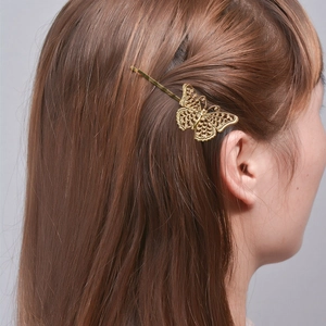 Elegante gouden vlinder haarspeld met filigraan ontwerp gedragen door een vrouwelijk model