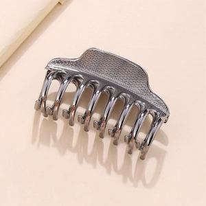 Détail macro d'une pince à cheveux en métal gris foncé avec texture grillagée et dents