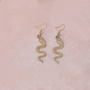 Boucles d'oreilles serpent dorées avec yeux en gemmes bleues sur un fond texturé