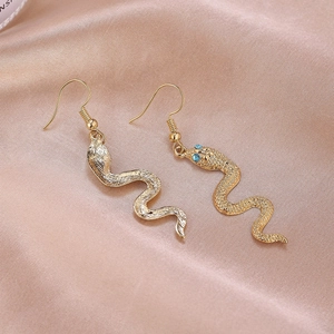 Boucles d'oreilles serpent dorées avec yeux en cristal bleu sur satin rose élégant
