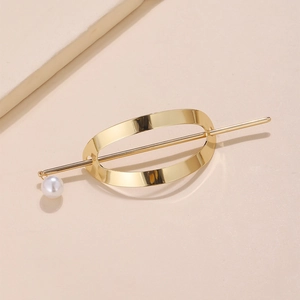 Minimalistische goldene Haarspange aus Metall mit einer weißen Perle auf beigem Grund