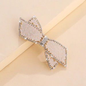 Elegante fermaglio a fiocco dorato con perle e strass luccicanti su sfondo di tessuto beige