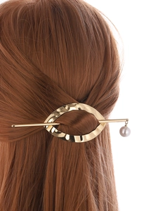 Close-up of golden geometric hair stick set with pearl pendant on brown hair